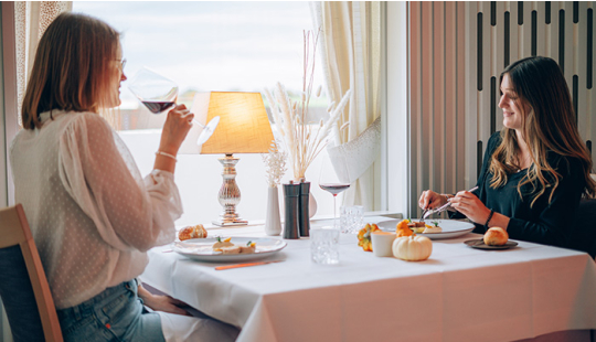 Zwei Frauen genießen im Restaurant Empire ihr Menü und ein Glas Wein. 