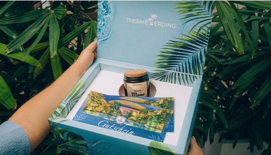 Geschenkbox mit blauem Hintergrund und Palmen, gefüllt mit zwei Gutscheinen und einer Kerze mit der Aufschrift "Beste Mama"