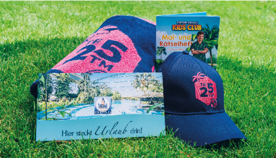 Geschenkumschlag, Cap mit pinkem Logo "TE 25 TM", Handtuch mit pinkem Logo "TE 25 TM" und Therme Erding Kids Club Mal- und Rätselheft liegen im Gras
