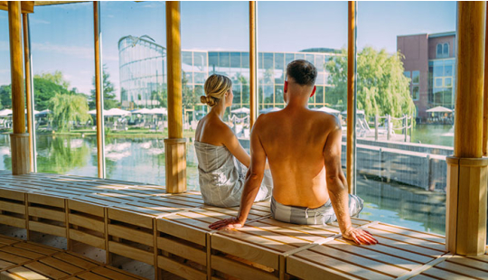 Ein Paar sitzt in einer Sauna mit Panoramaausblick auf den Natursee