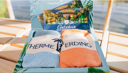 Eine Geschenkbox mit zwei Hamamtüchern, eins in orange und eins in blau. Zusätzlich sind zwei Gutscheine für die Therme Erding zu sehen.